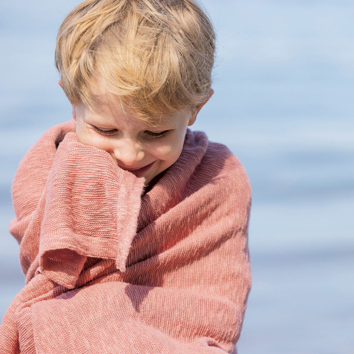 Child wrapped in a pink linen cotton blanket with a blurred blue background
