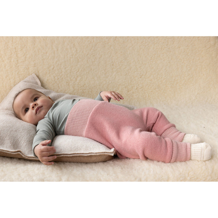 Baby lying on a cushion wearing a pink wool pants