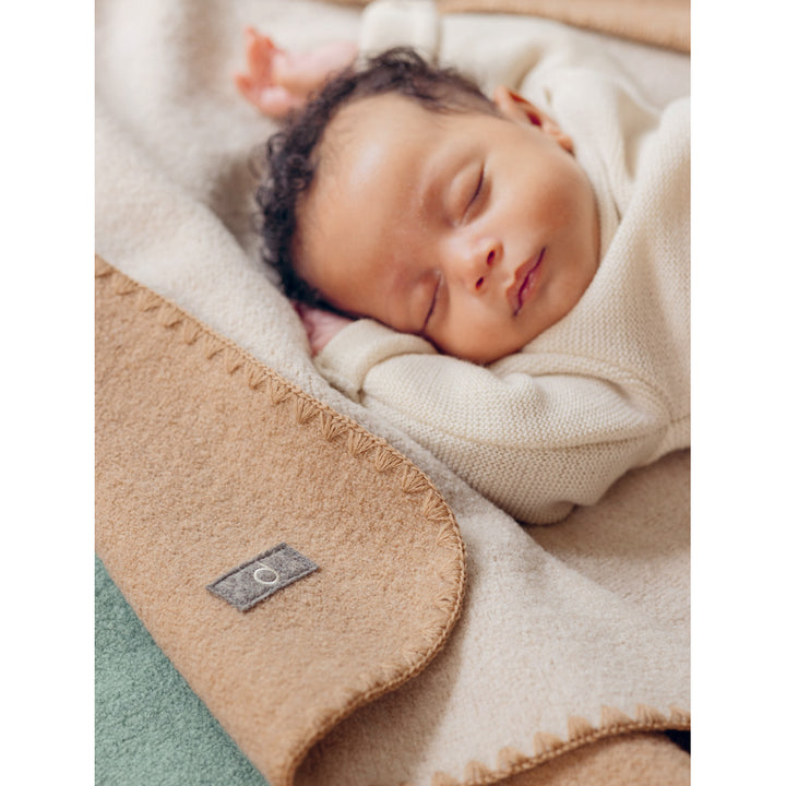 Newborn baby sleeping under a caramel doubleface organic wool  blanket with a Disana label