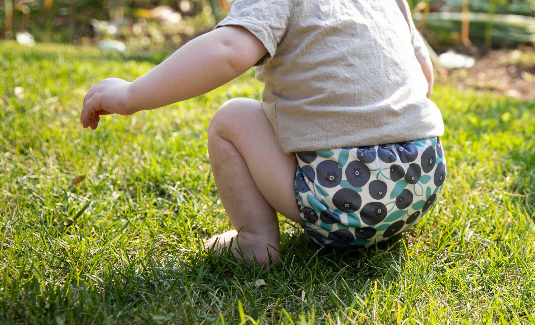 Child wearing a Thirsties cloth diaper with a blueberry pattern on grass