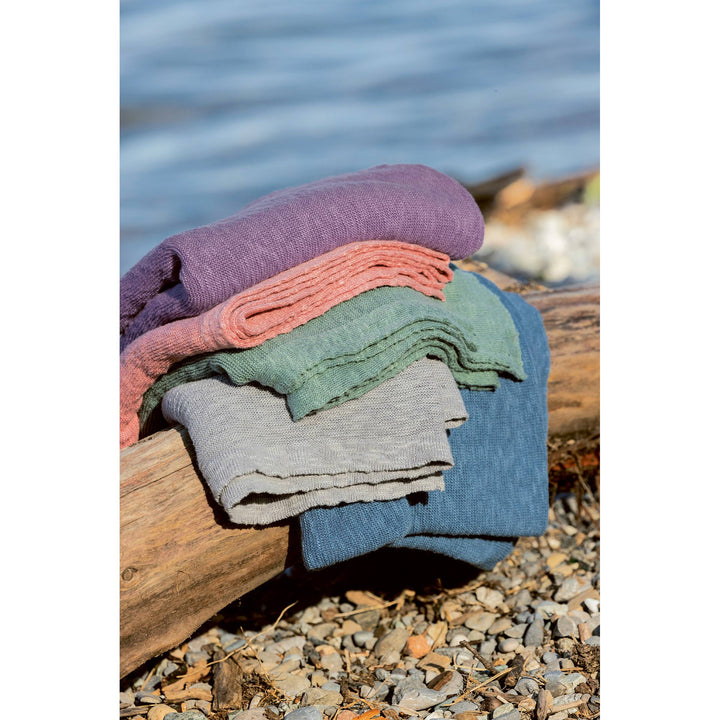 Stack of colorful linen blankets on a log by a body of water