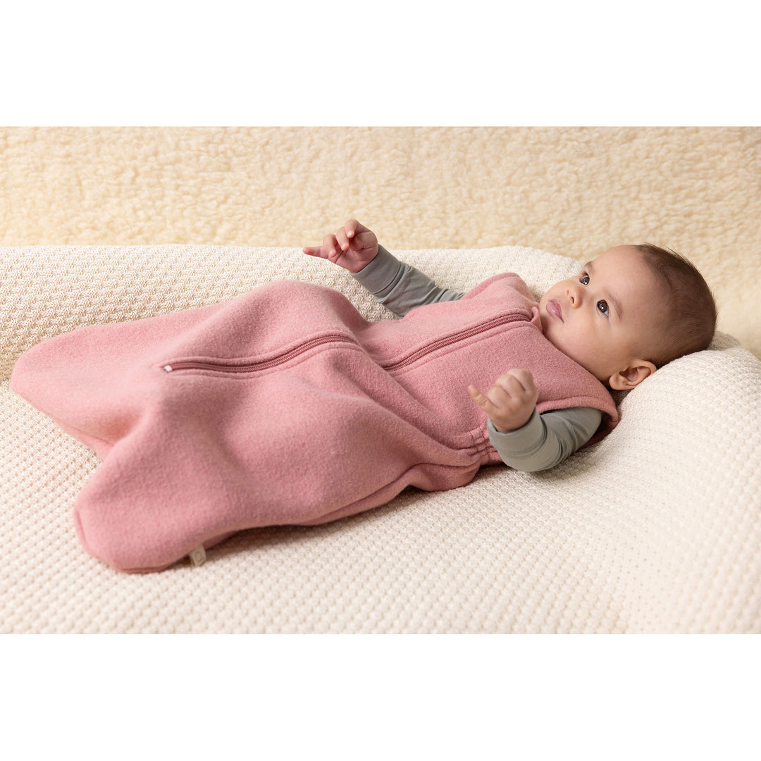 Baby in a pink sleeping bag lying on a natural wool blanket