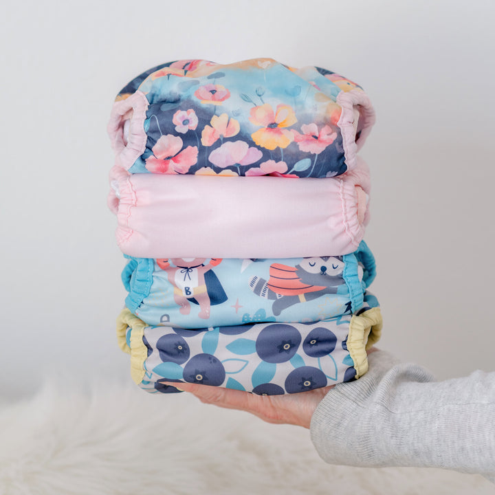 Stack of colorful  Thirsties cloth diapers held by a person against a light background