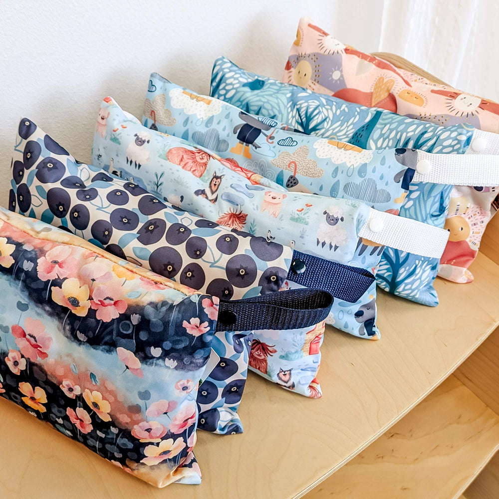 Set of colorful Thristies mini wet bags for cloth diapers with various patterns on a wooden surface.