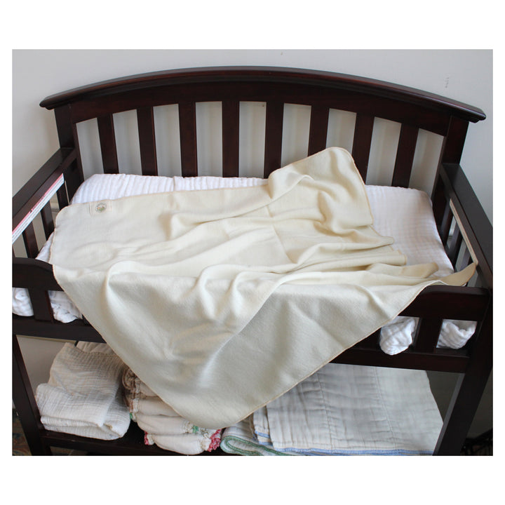 Wool swaddle blanket draped over a dark brown wooden changing crib, with white muslin cloths stacked underneath.