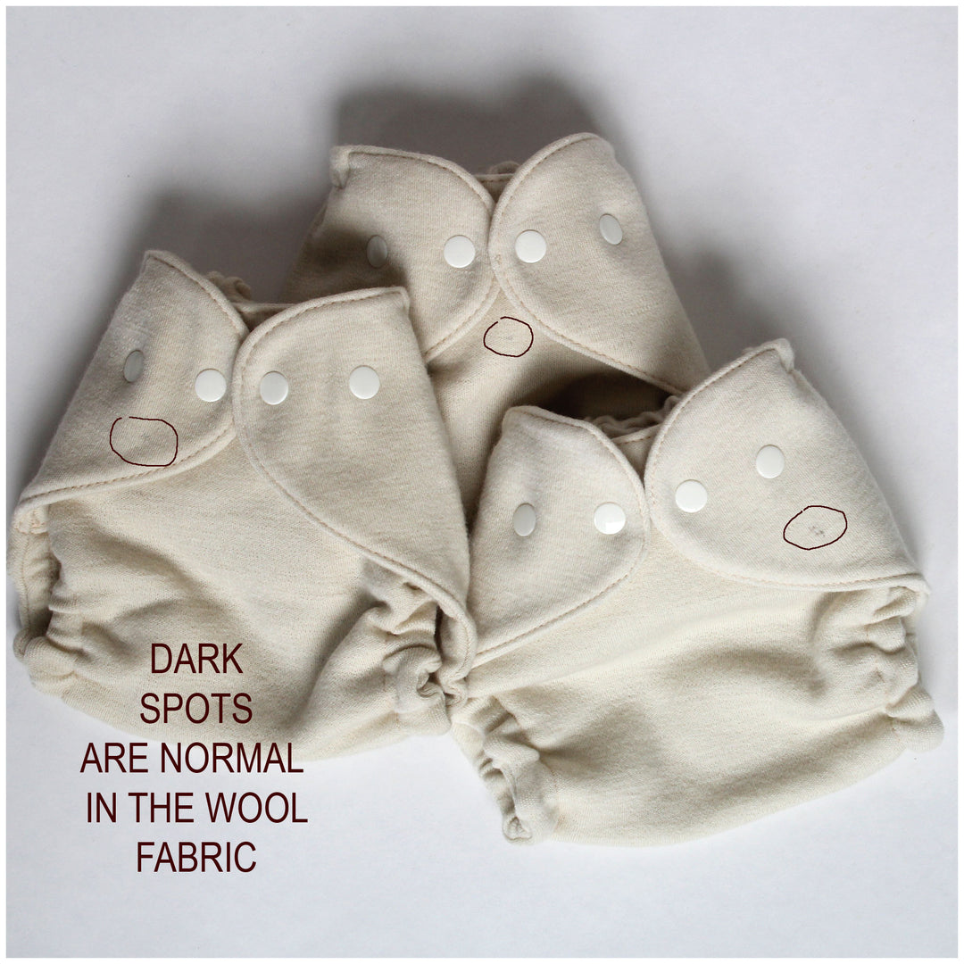 wool cloth diaper covers with white snap closures, arranged on a light gray background. The image includes a text overlay explaining that dark spots are normal in the wool fabric.