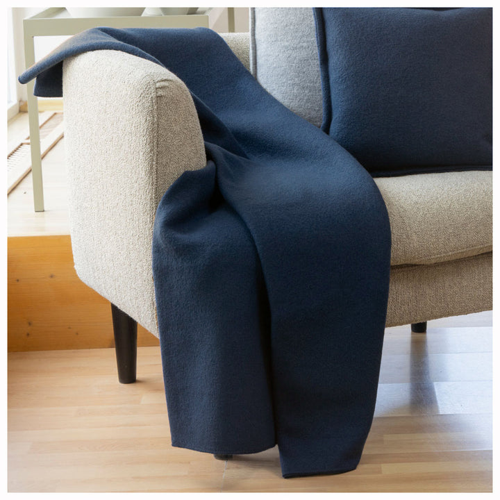 Navy blue wool blanket draped over a beige armchair on a wooden floor.