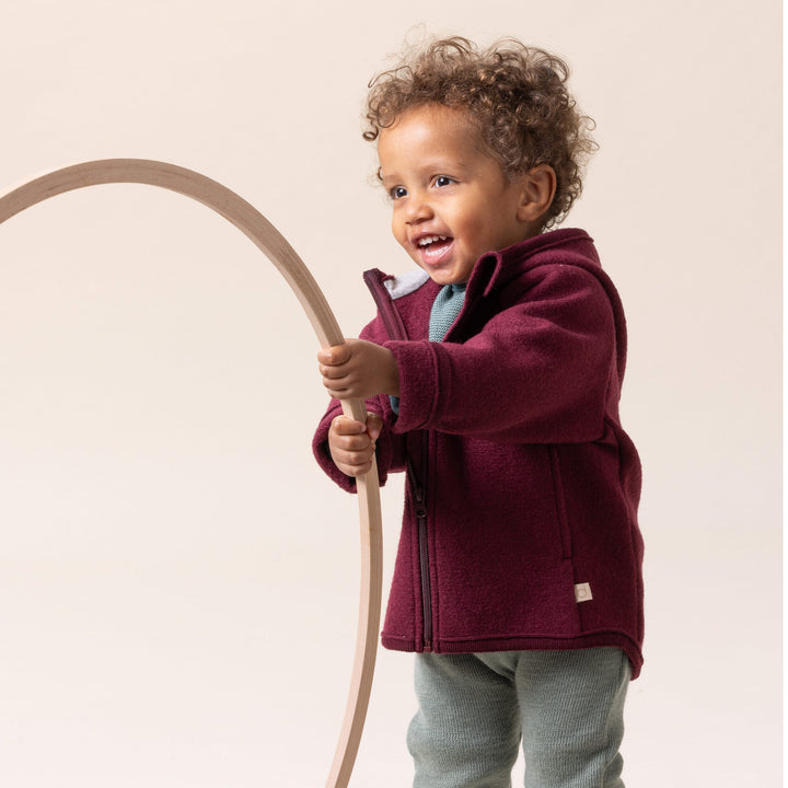 Child wearing a Cassis Disana organic merino wool jacket holding a wooden hoop 