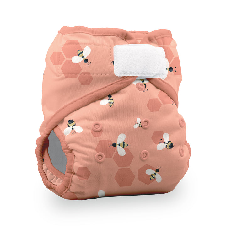 Thirsties pocket diaper Let it Bee print reusable cloth diaper in a dusty peach-pink color, decorated with a pattern of honeycomb hexagons and bumblebees. It features a white hook-and-loop fastener